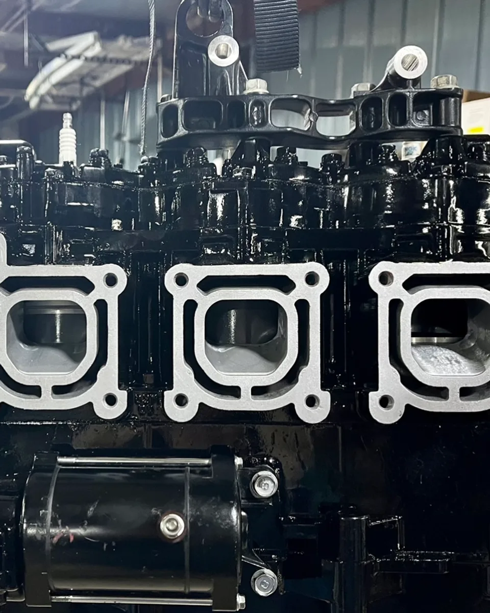 A rebuilt three-cylinder powerhead hanging in a lift strap on the shop bench at All Seasons Repair Service in Stevens Point