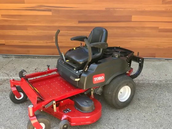 A Toro zero-turn riding mower photographed on a concrete apron against cedar siding